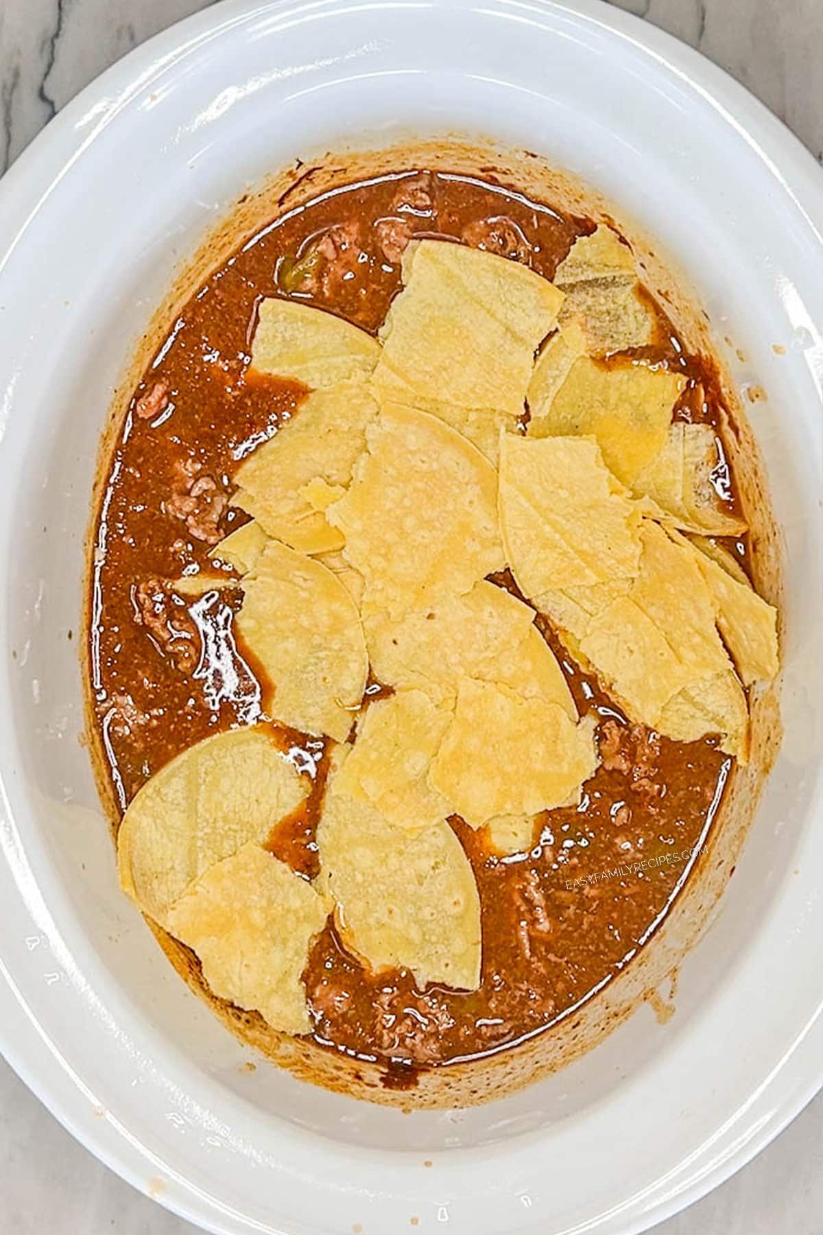 torn up corn tortilla layered on top of beef enchilada filling.