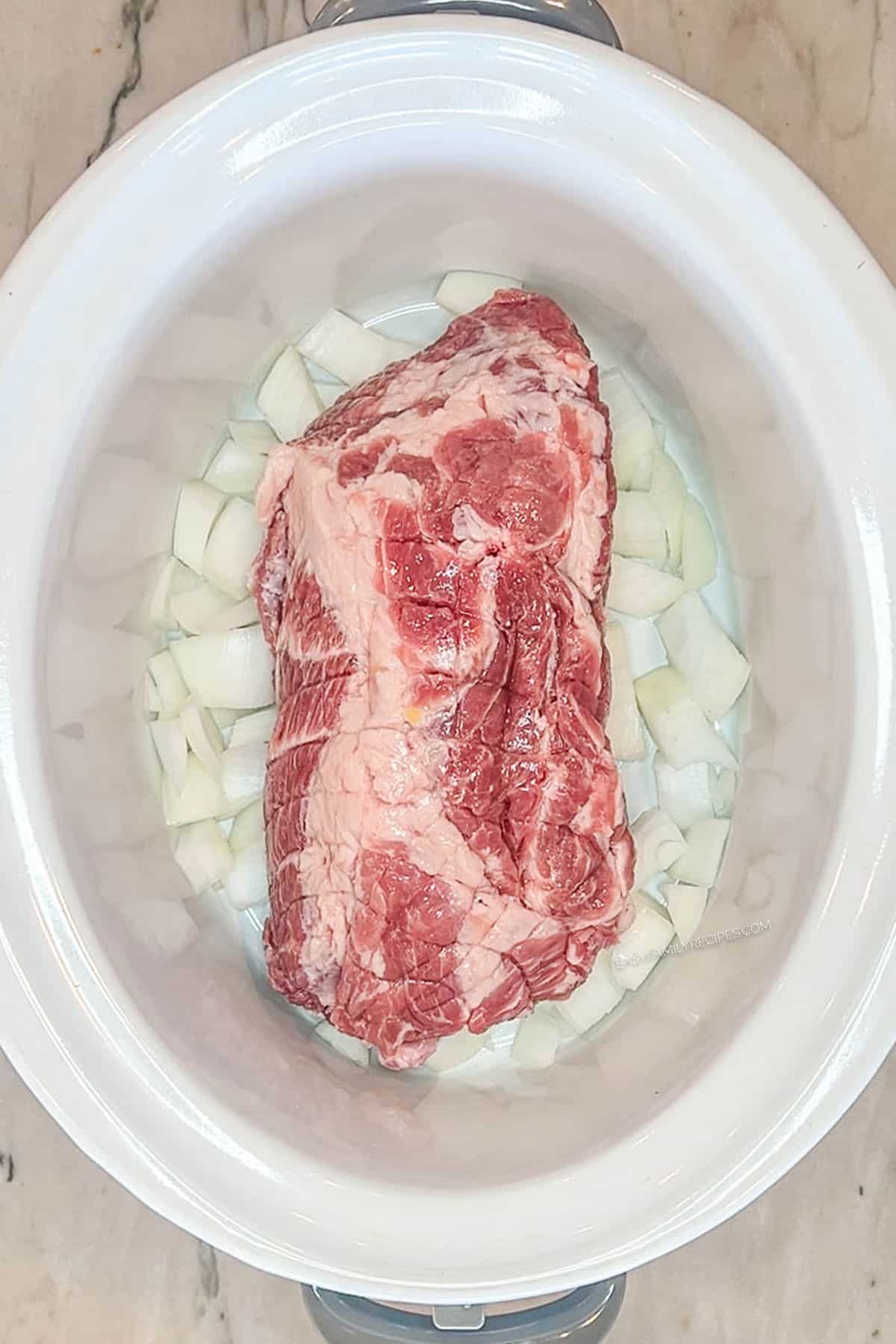 Pork shoulder in the crockpot with onions.