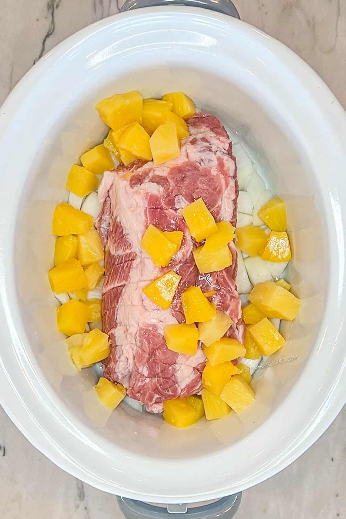 Pork shoulder in a slow cooker with onion and pineapple chunks.