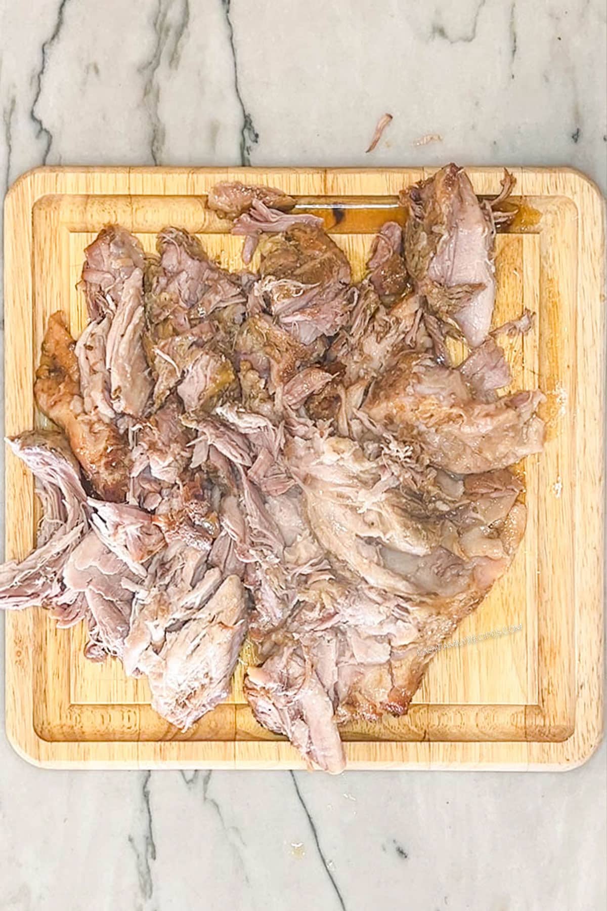 Shredding the cooked pork shoulder on a wooden cutting board.