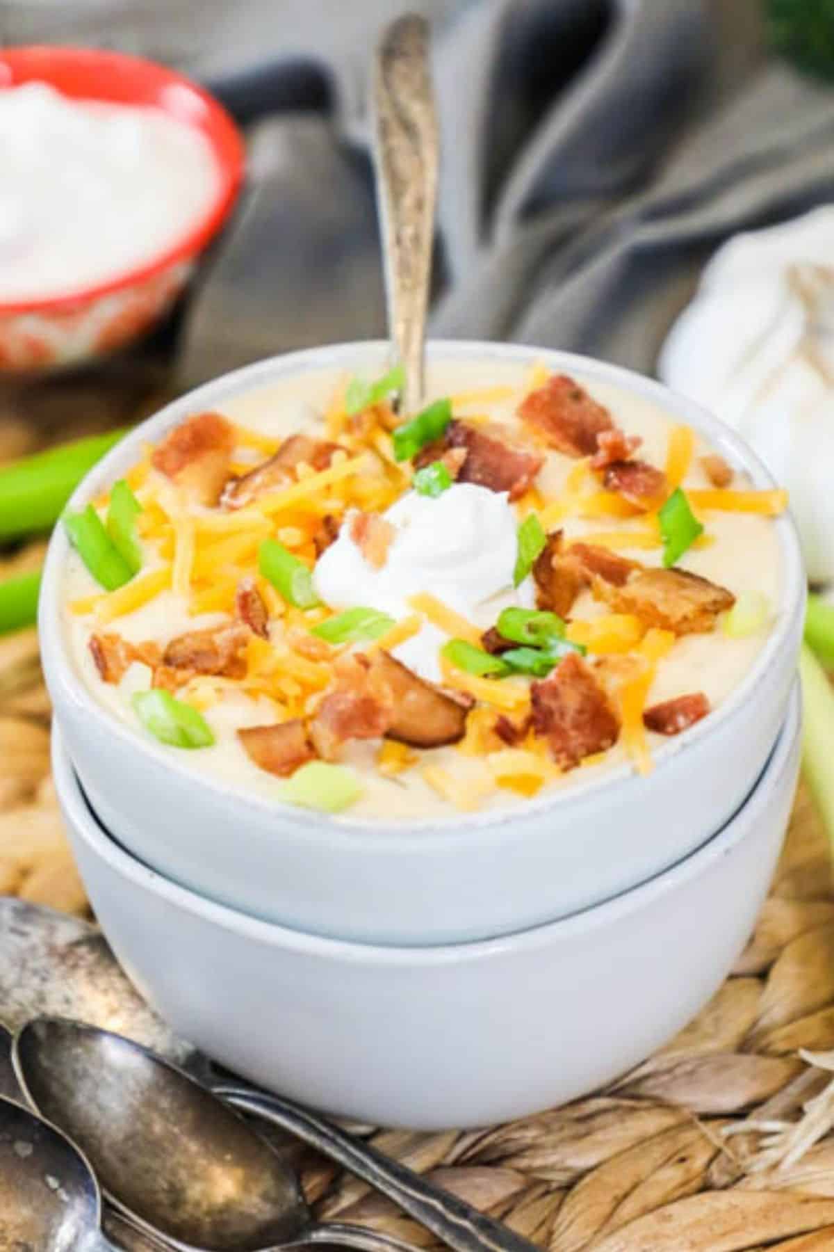 bowl of baked potato soup topped with bacon, cheese, scallions, and bacon.