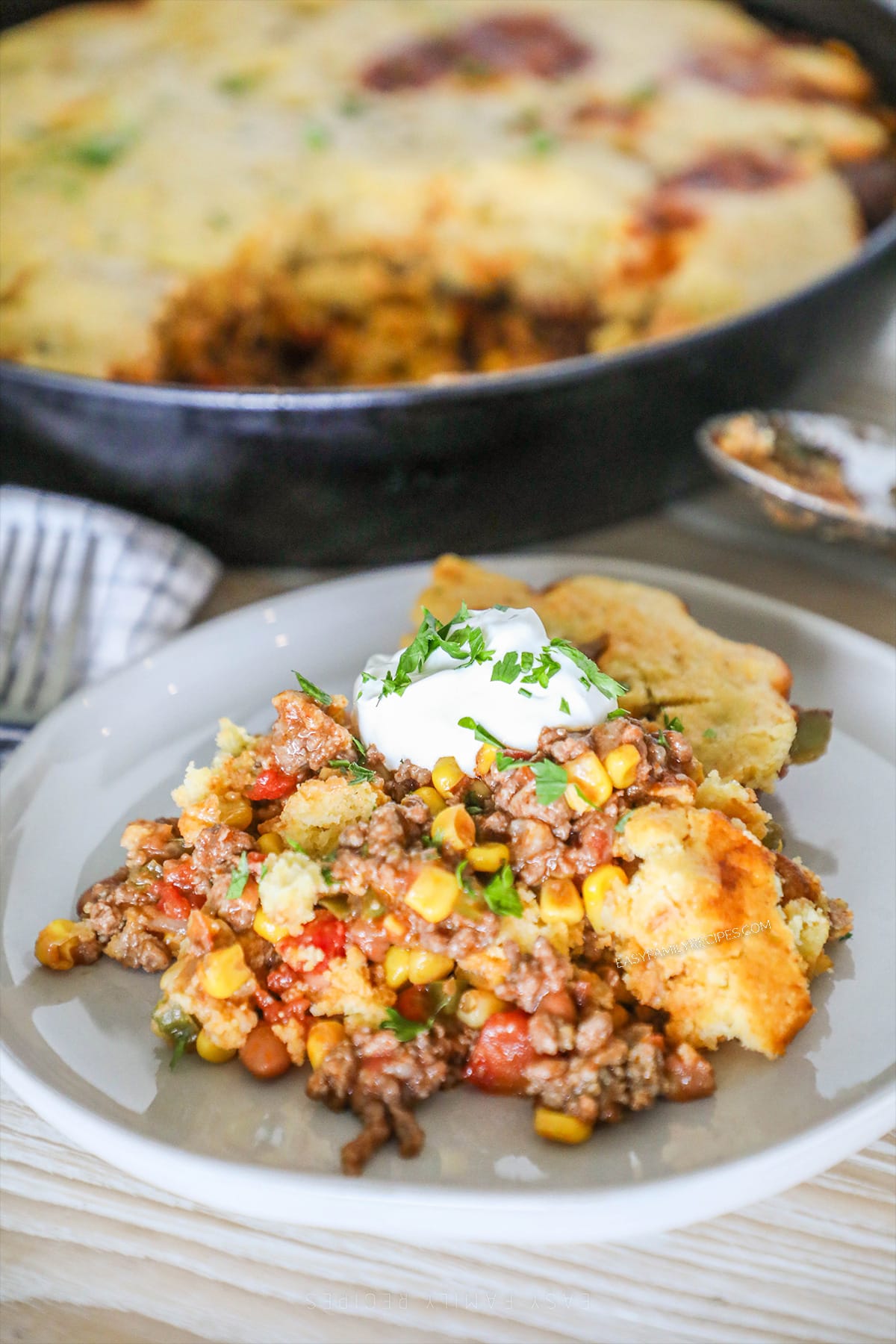 A serving of cowboy casserole with sour cream and cilantro on a white plate.