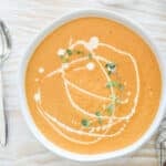 Top view of roasted veggie soup in a white bowl on a distressed wood background
