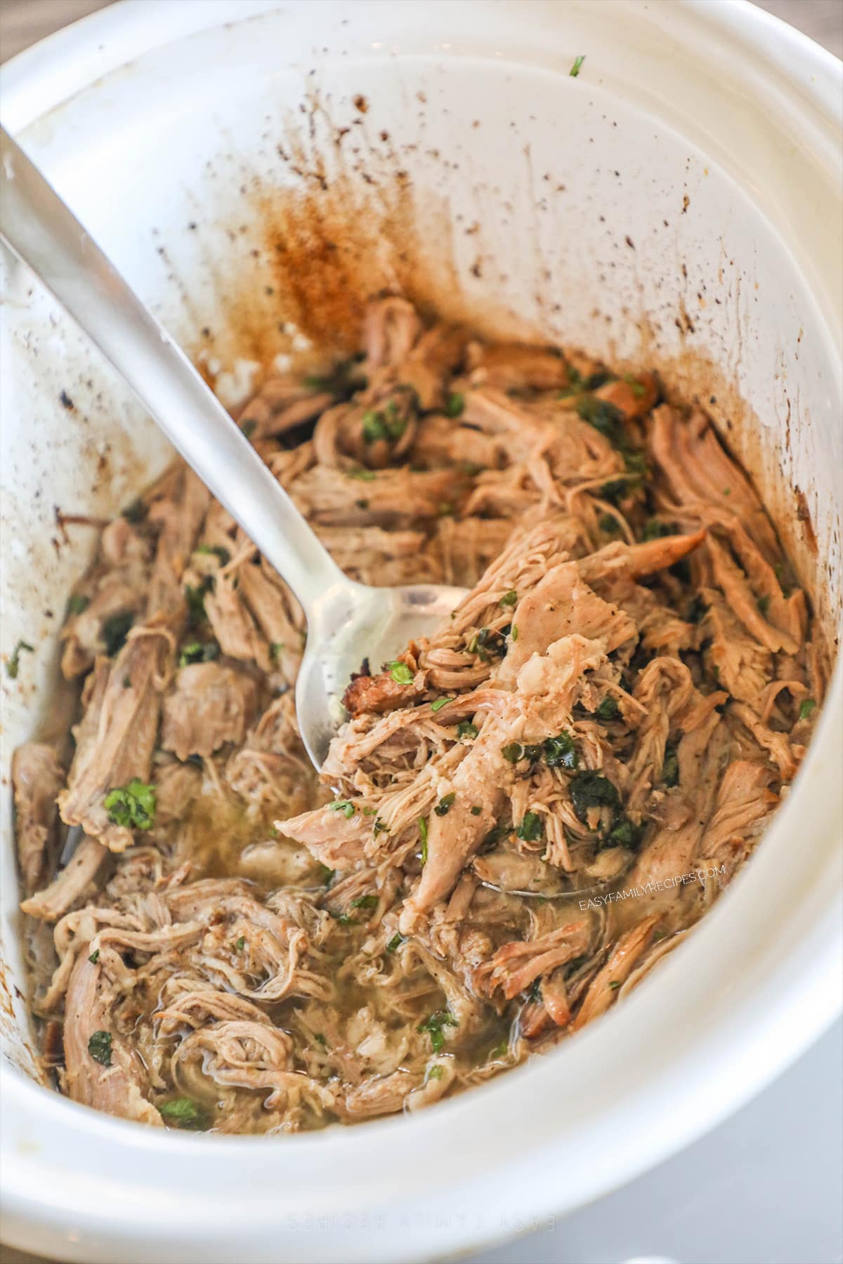 Crockpot Cuban Style Mojo Pork in a slow cooker with a silver serving spoon