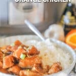 Crockpot Orange Chicken on a white plate with rice and a slow cooker in the background. The text reads, “Crockpot Orange Chicken”
