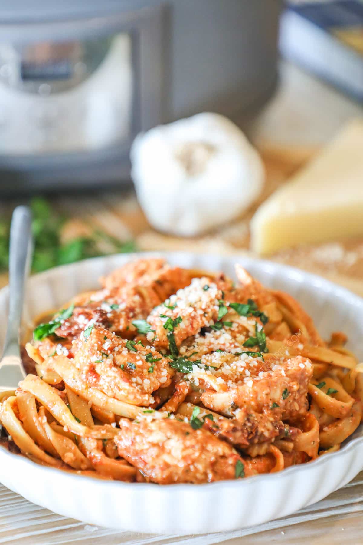 Crockpot Sun Dried Tomato Chicken Alfredo in a white bowl with parmesan and parsley garnish