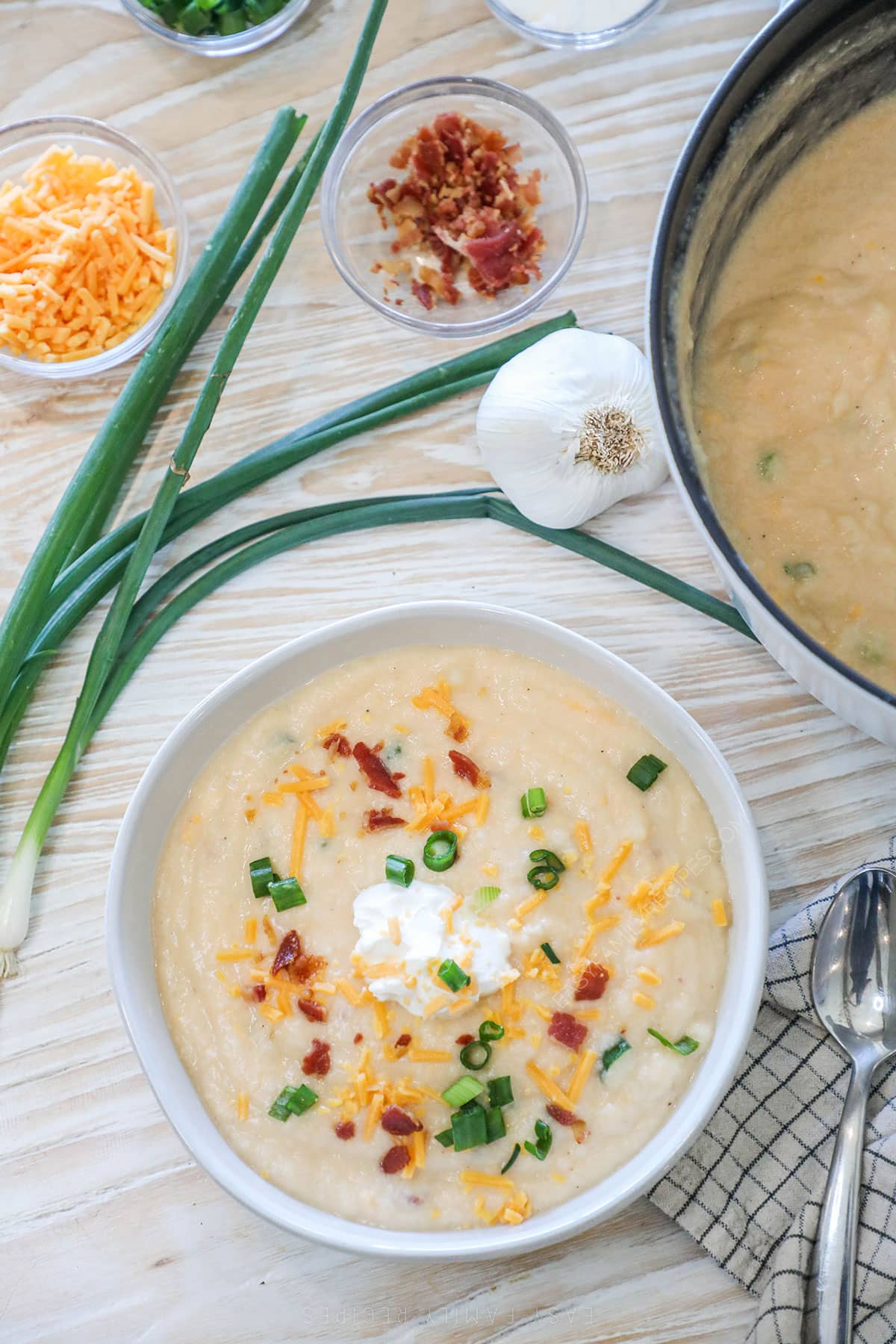 Overhead shot of a bowl of cauliflower soup next to toppings like cheese and bacon bits.