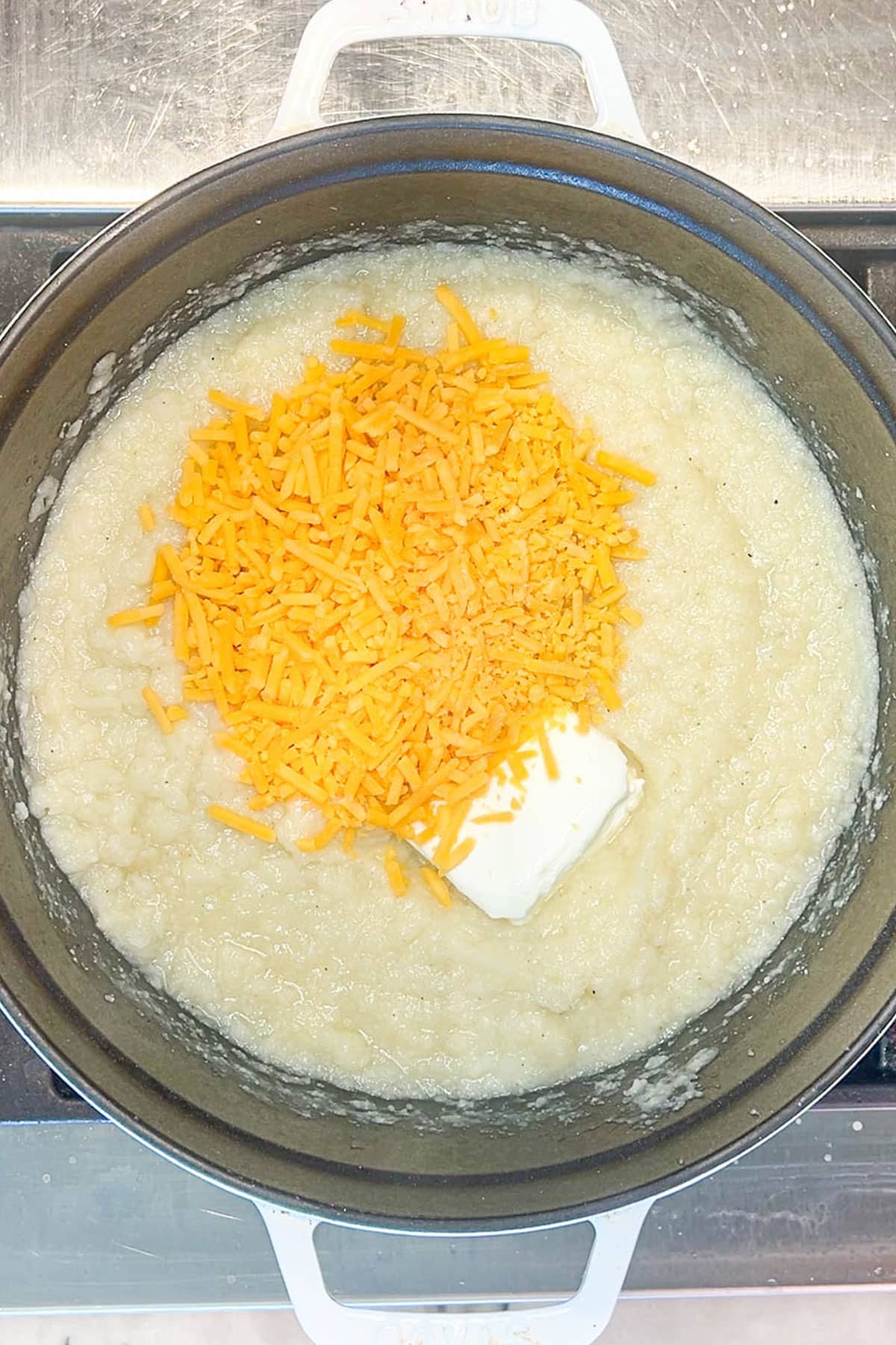 Shredded cheese and butter added to cauliflower mixture in a pot.