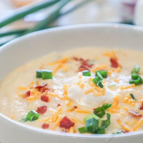 Side view of a bowl of cauliflower soup topped with cheese, bacon, sour cream and green onions.