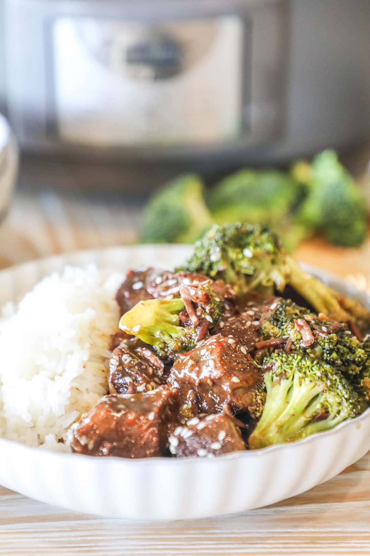 Crockpot Beef and Broccoli over rice in a white bowl with a slow cooker in the background