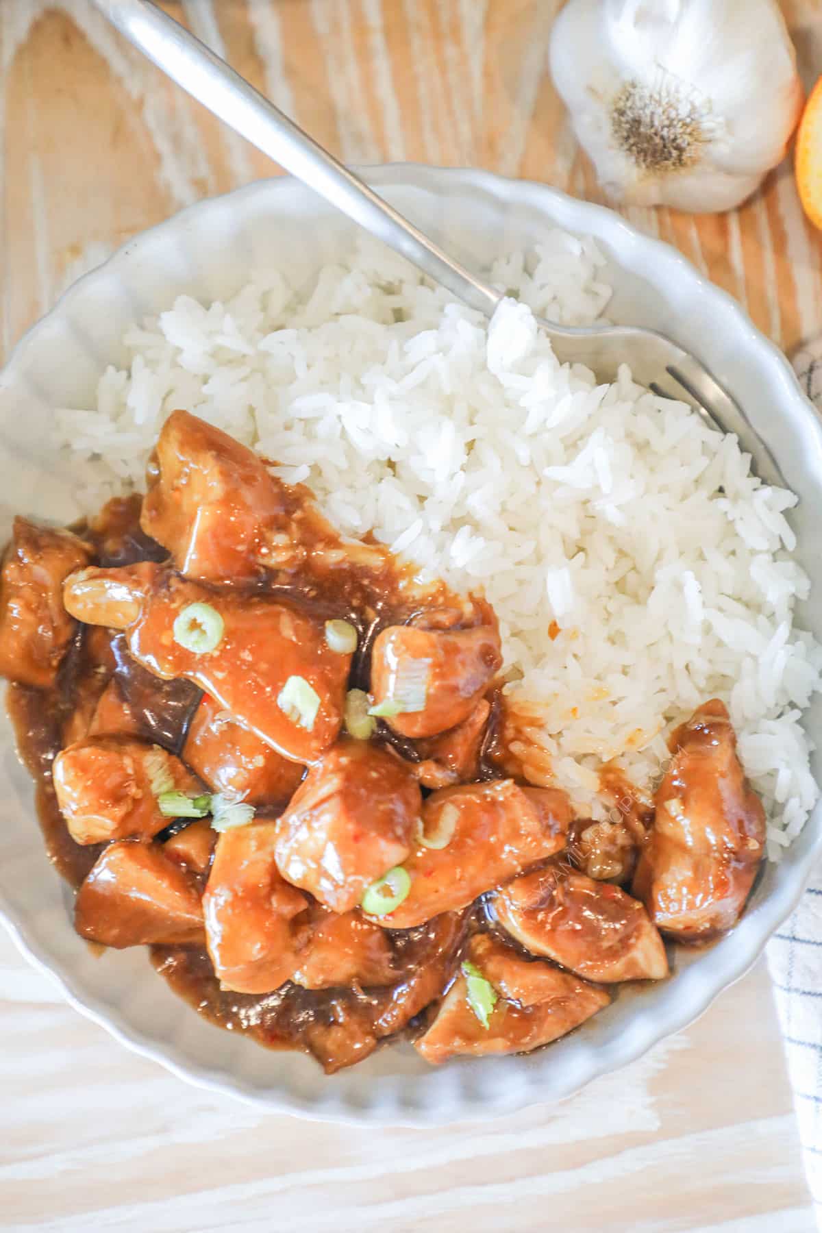 A serving of Crockpot Orange Chicken in a white bowl with rice. Scallions garnish the dish.