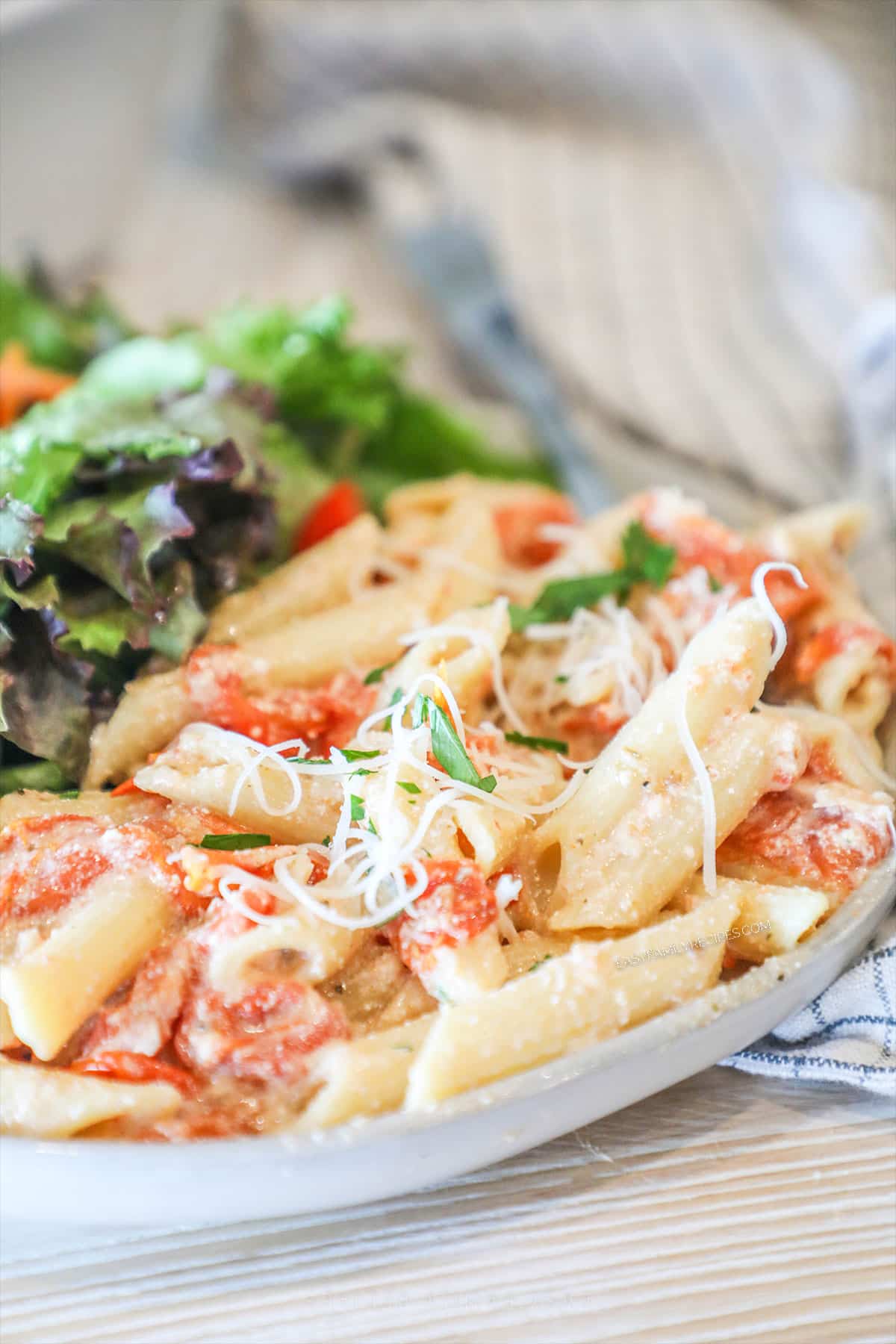 a side view of a plate piled with tomato and ricotta pasta and a side salad.