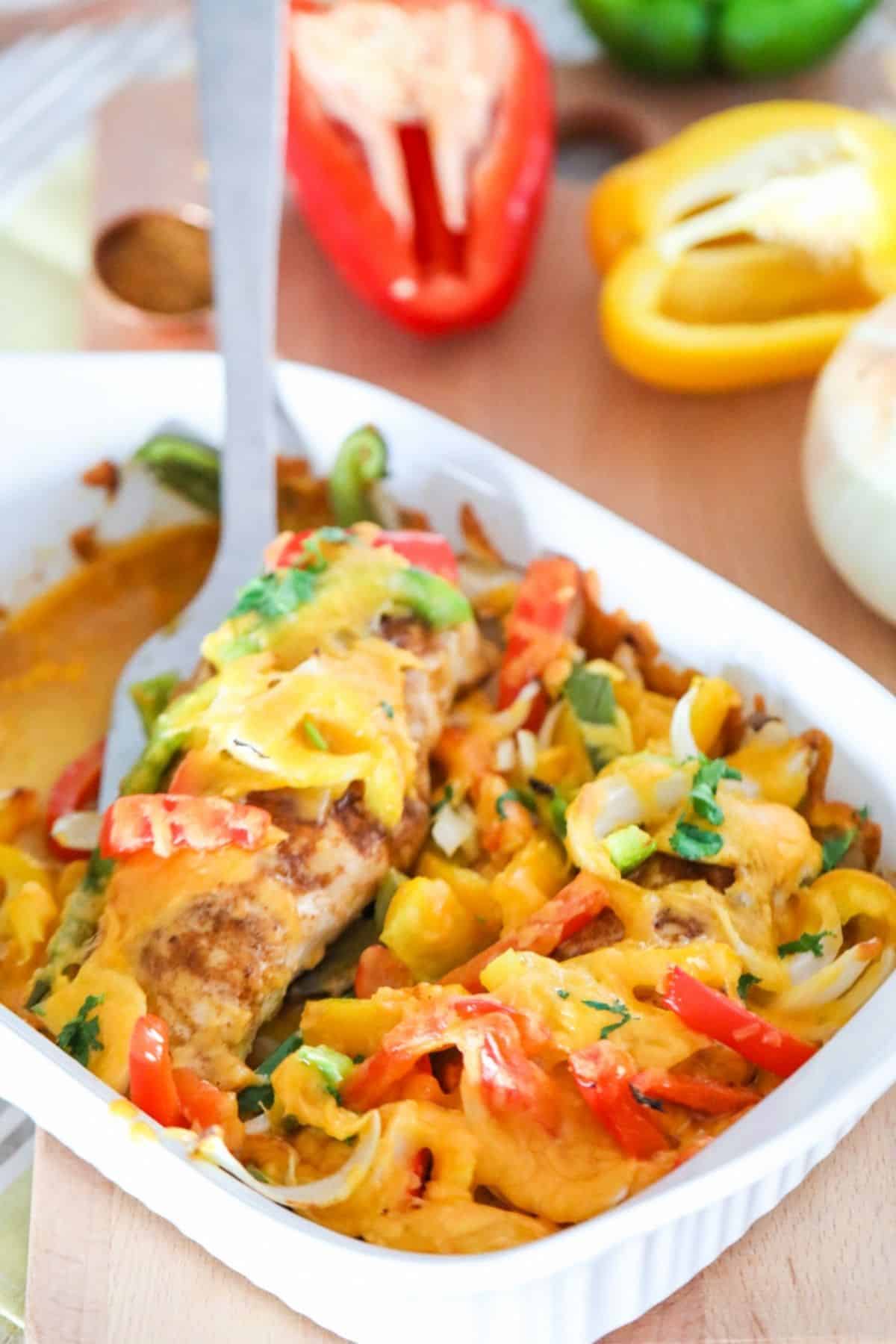chicken breasts topped with onions peppers and cheese in a white casserole dish