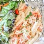 above image of tomato ricotta pasta on a plate with a side salad.