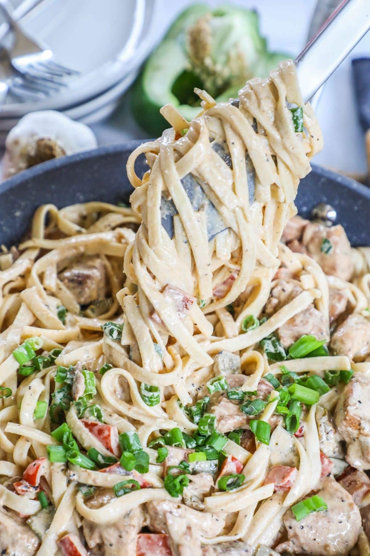 tongs lifting a scoop of cajun chicken pasta from the skillet