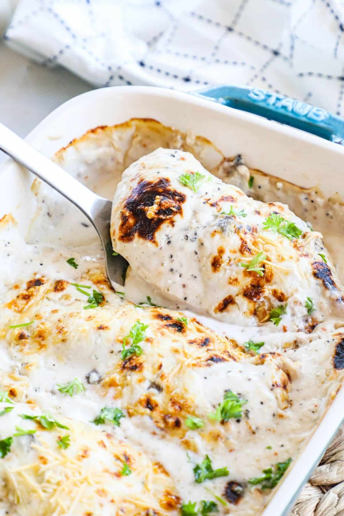 creamy mushroom chicken breast being lifted from baking dish on spatula