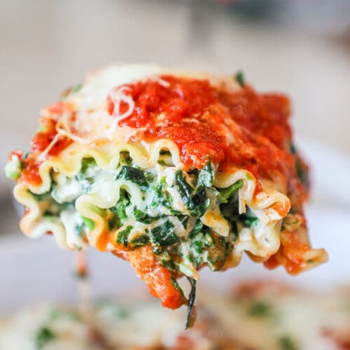 Side view of a spinach chicken lasagna roll up hovering over the rest of them in a baking dish.