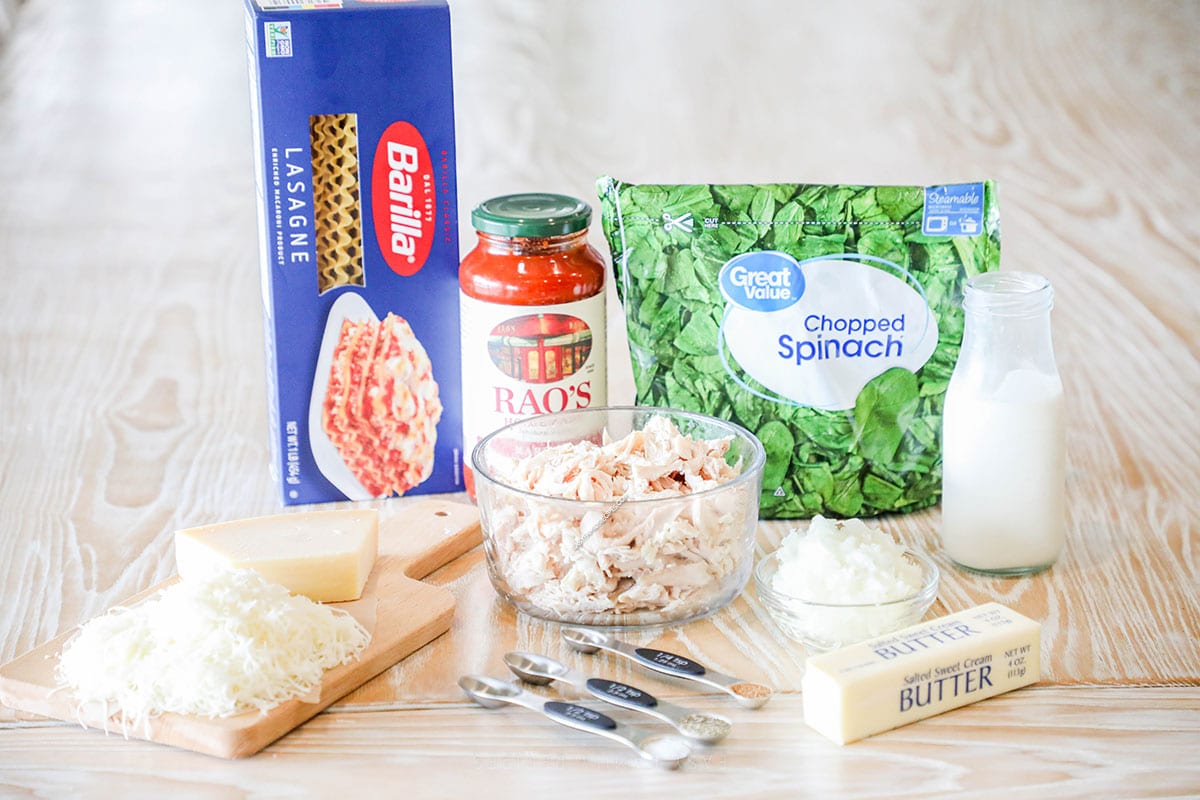 Ingredients needed to make creamy spinach chicken lasagna rolls ups lined up on a wooden background.