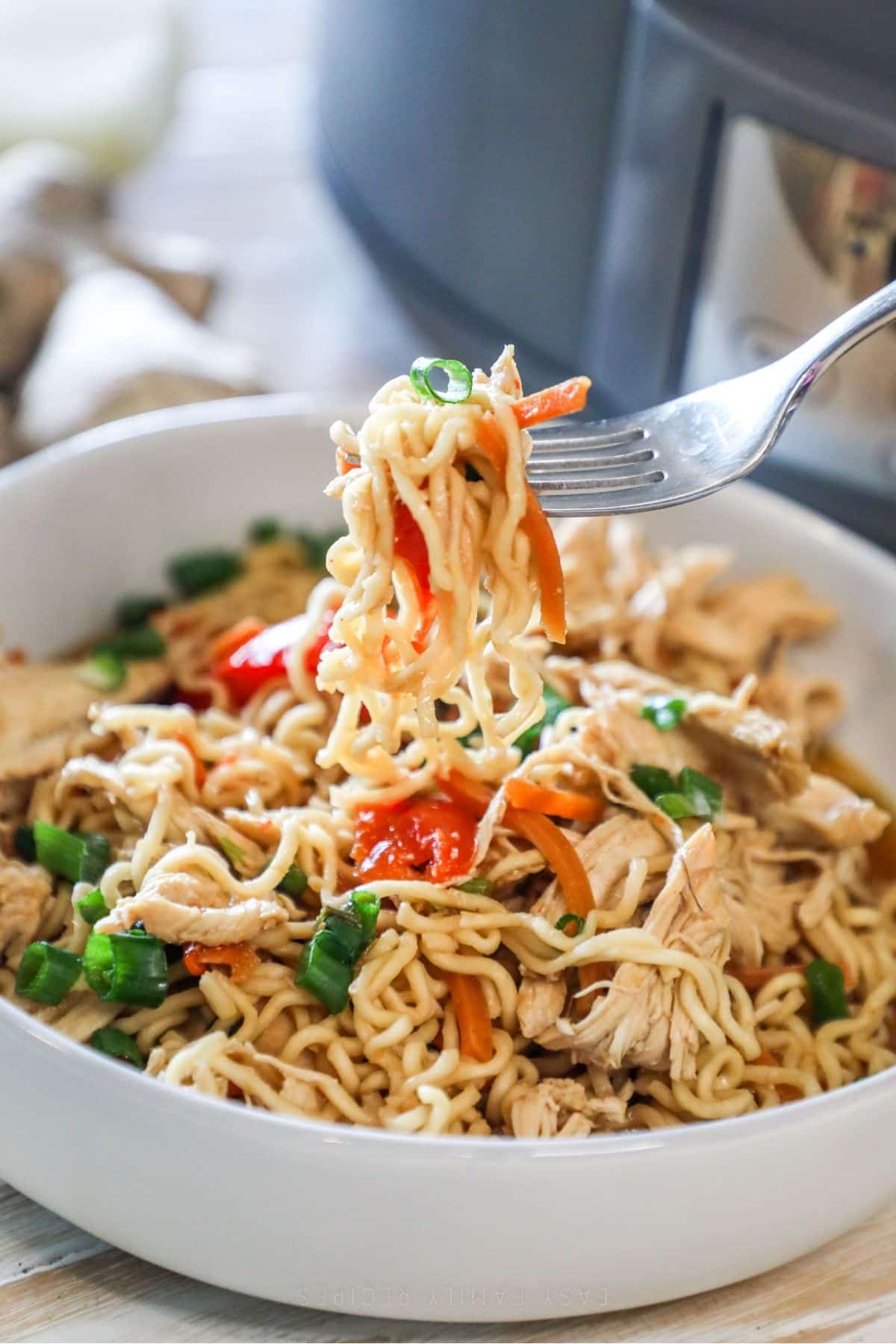 a scoop of crockpot chicken ramen being scooped from a white bowl