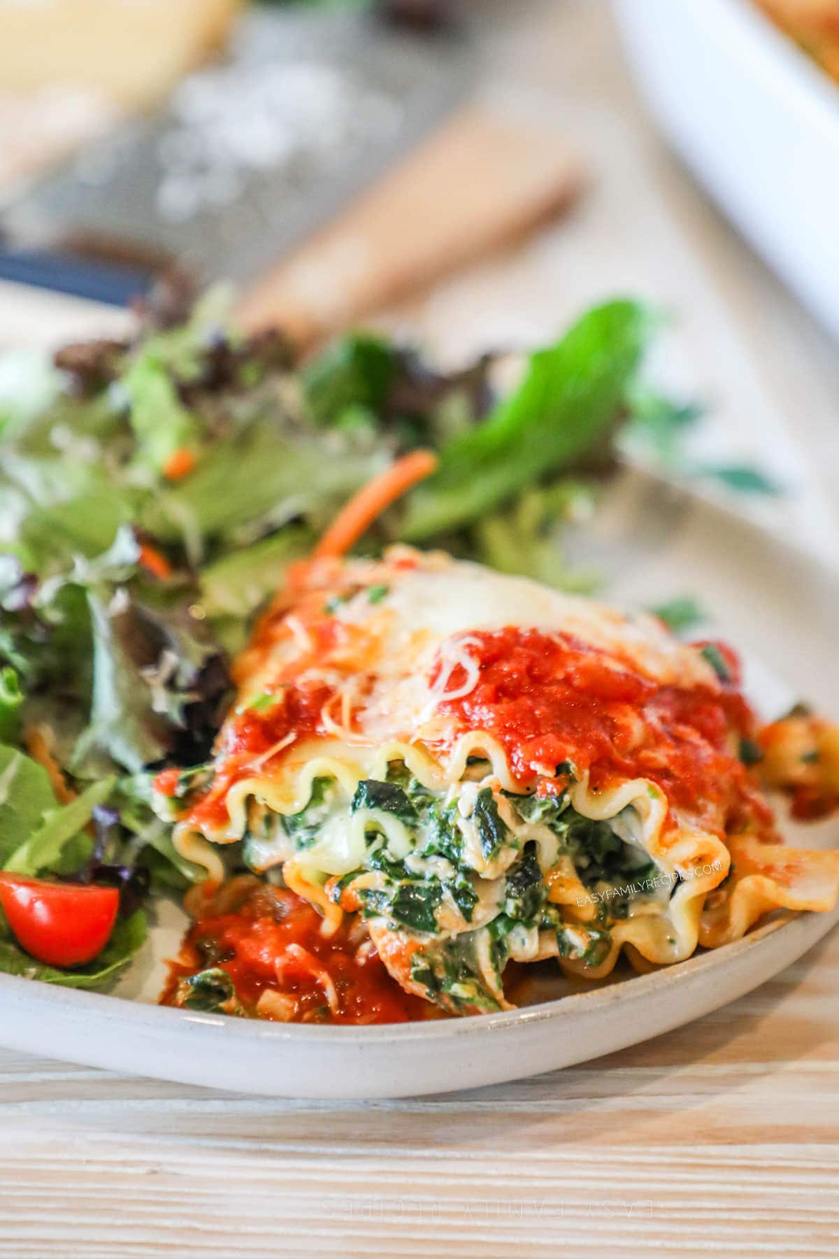 One spinach chicken lasagna roll up served on a plate with a side salad.