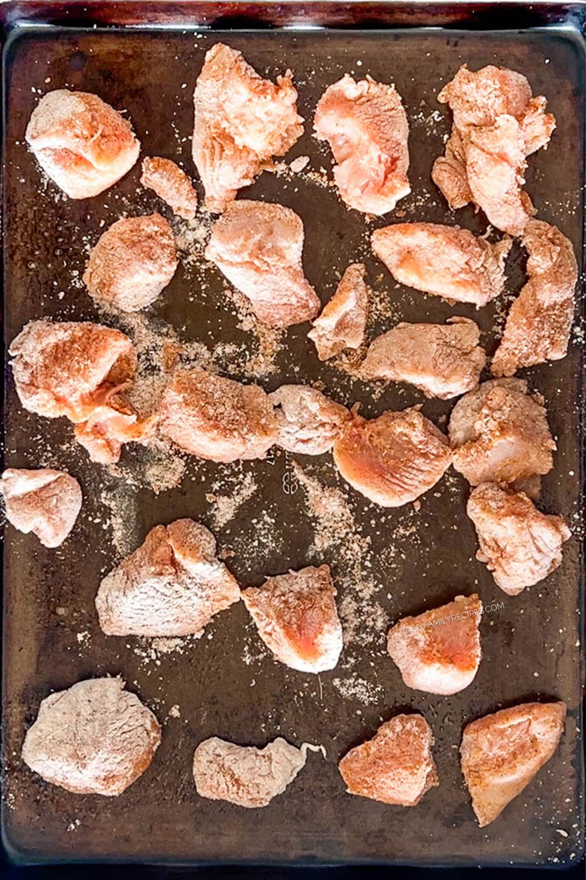 Coated chicken pieces placed on a sheet pan.