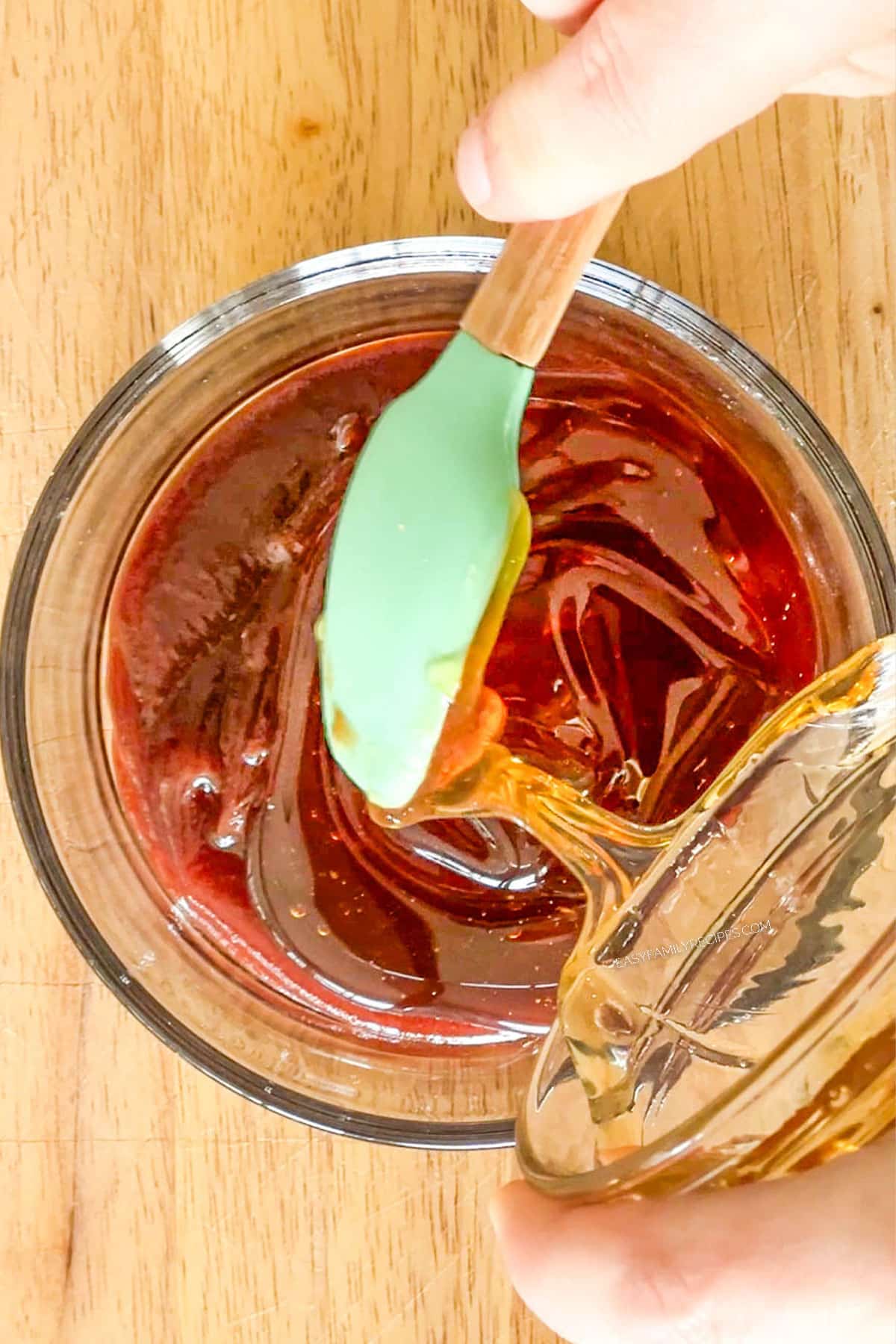 Pouring honey into BBQ sauce in a bowl.