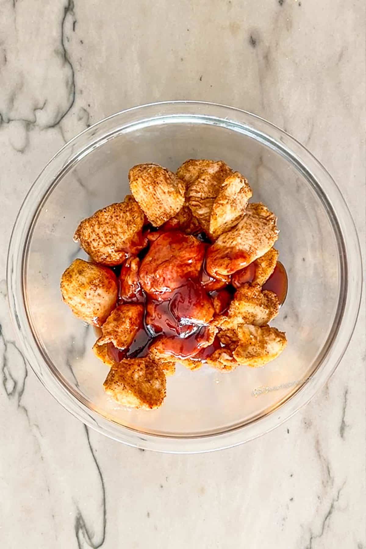 Coating the pieces of baked chicken with the honey BBQ sauce in a bowl.