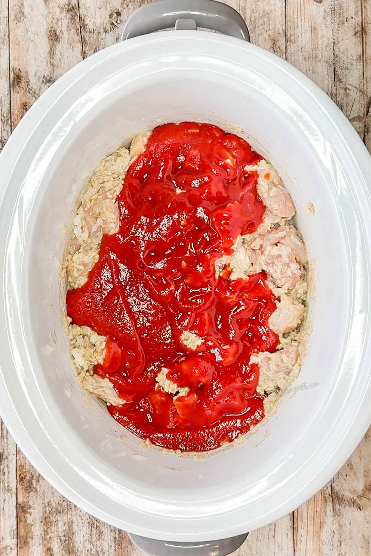 Tomato sauce poured on top of the chicken mixture in a slow cooker.