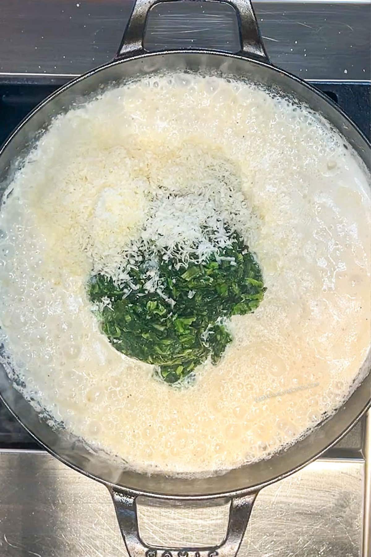 Creamy parmesan cheese sauce in a pan with frozen, drained spinach added.