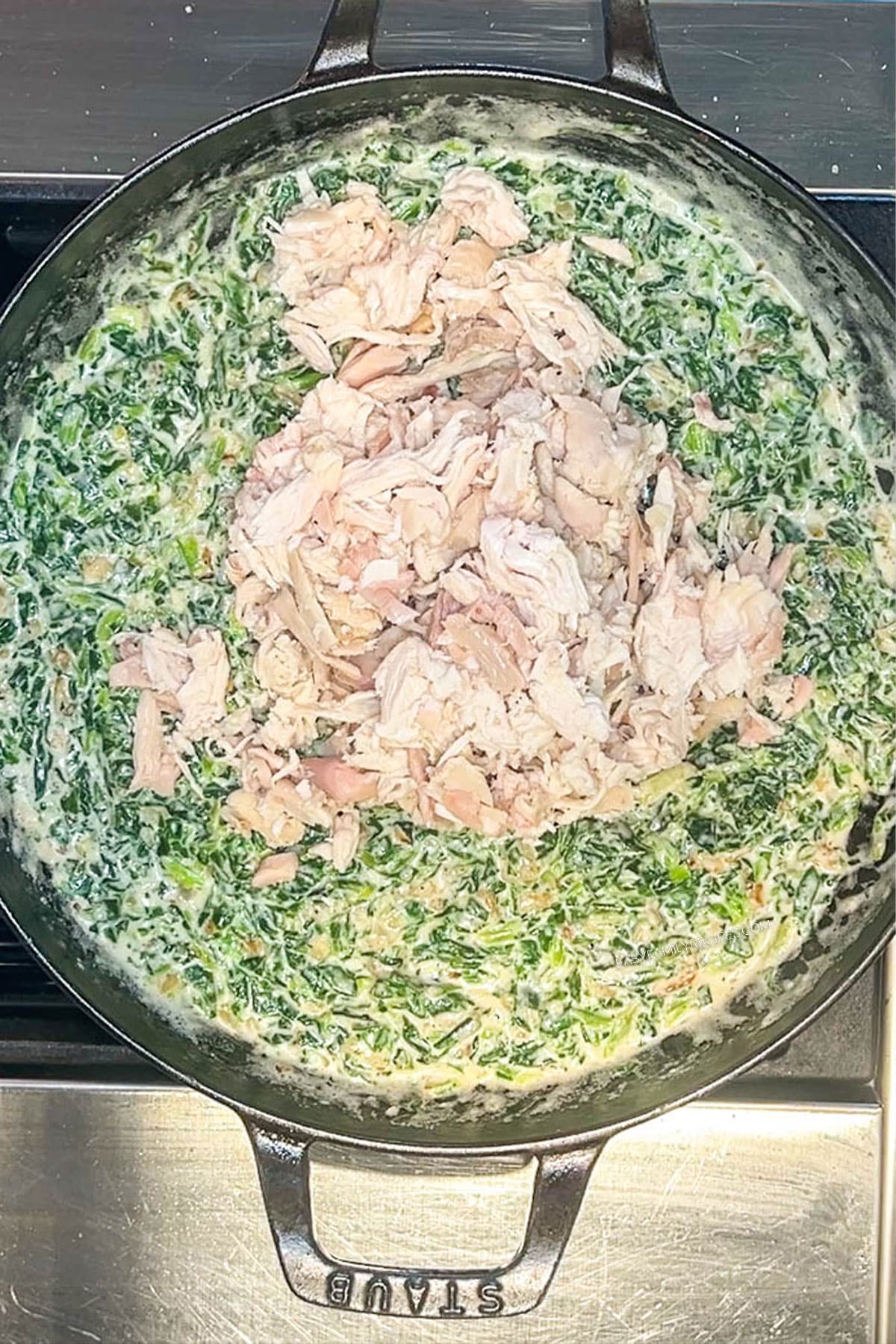 Shredded chicken added to the creamy spinach sauce in a skillet.