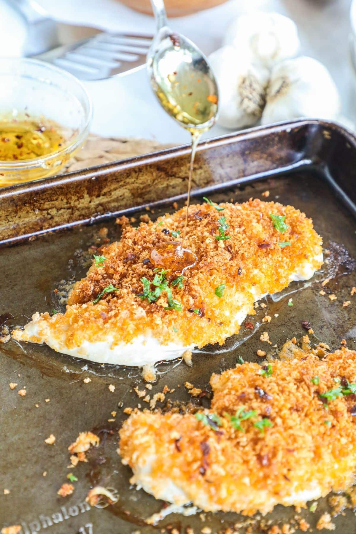 panko chicken breast on a baking sheet with a drizzle of honey being poured on top