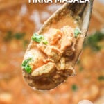 Spoonful of chicken tikka masala hovering over the rest of it in a crockpot.