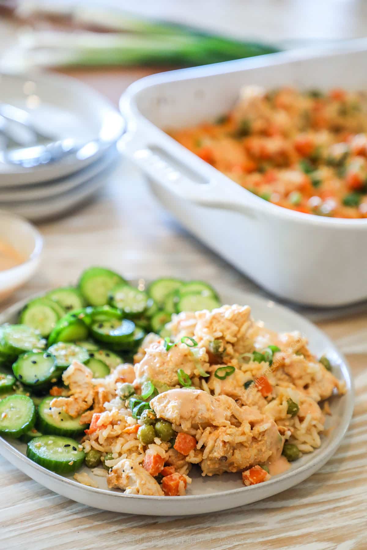 Portion of bang bang chicken bake on a plate with a side of cucumber salad.
