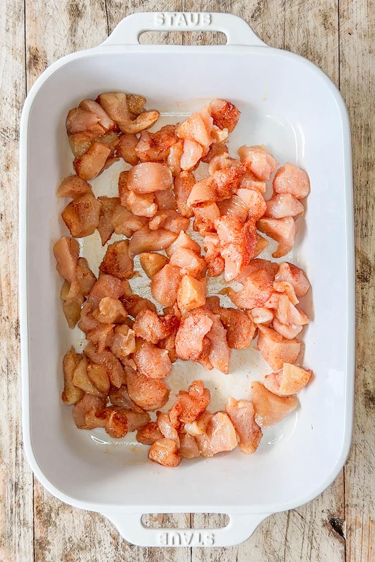 Diced and seasoned chicken in the bottom of a baking dish.