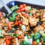 Sheet pan cashew chicken on a baking sheet with a spatula scooping some up.