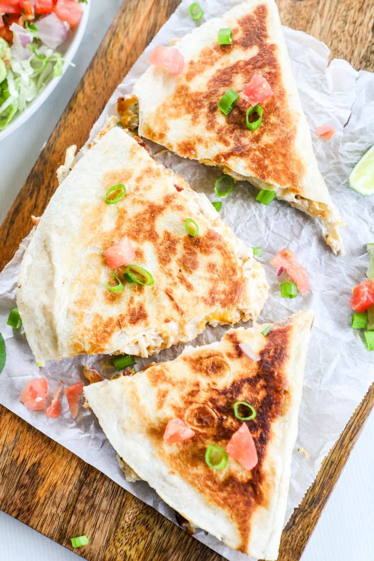 3 triangles of chicken bacon ranch quesadilla on a wooden cutting board