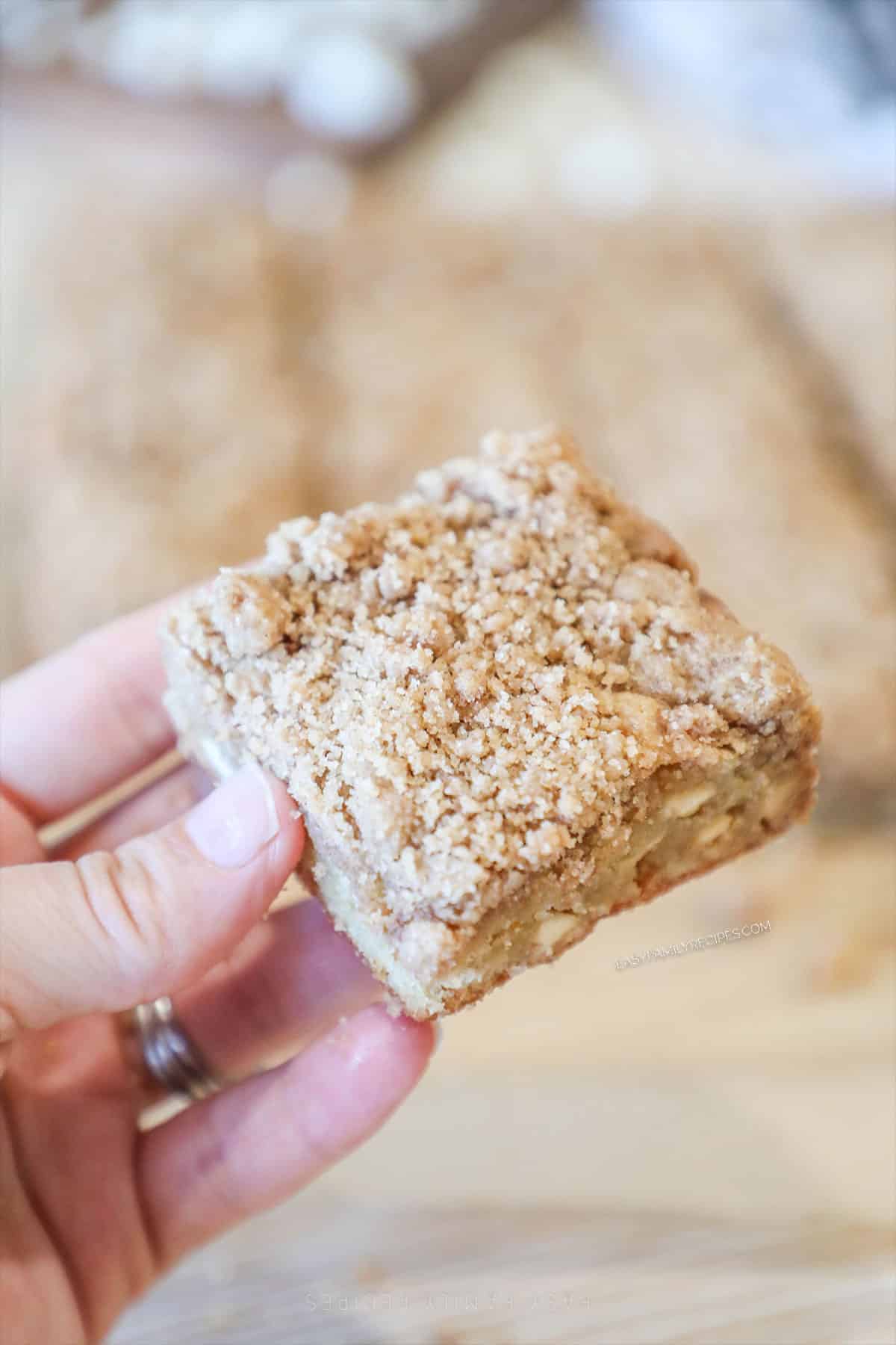 Hand holding a cinnamon streusel blondie with more bars in the background.