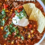 Close up of bowl of easy crockpot taco soup with a dollop of sour cream and two tortilla chips on top