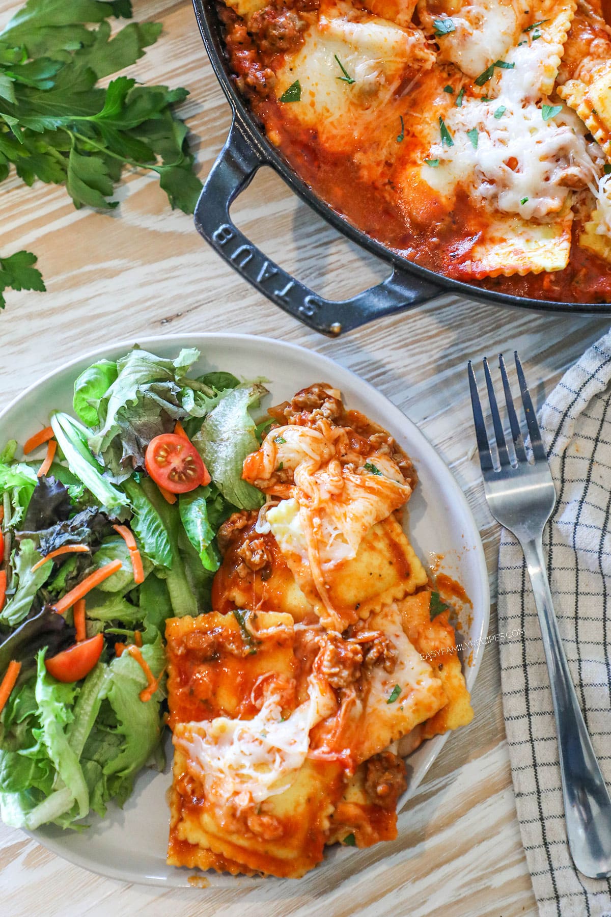 cheesy ravioli with sausage on a plate with a side salad.