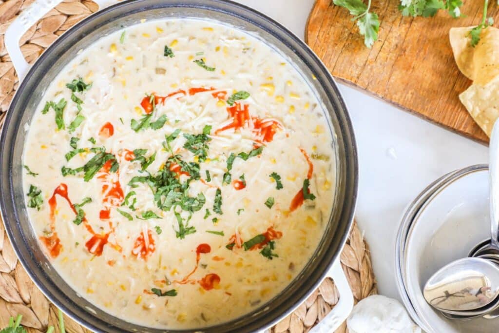 Pot of Green Chile Chicken Corn Chowder on a table garnished with cilantro and hot sauce.