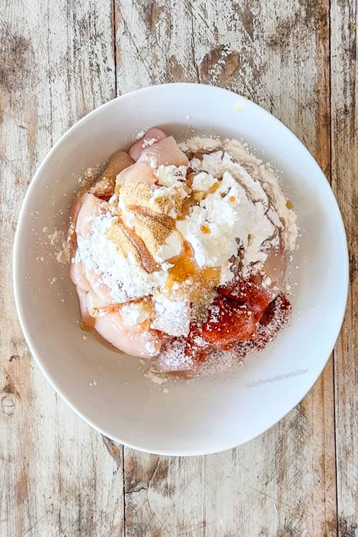 Spices and cornstarch added to the diced chicken breast in a mixing bowl.