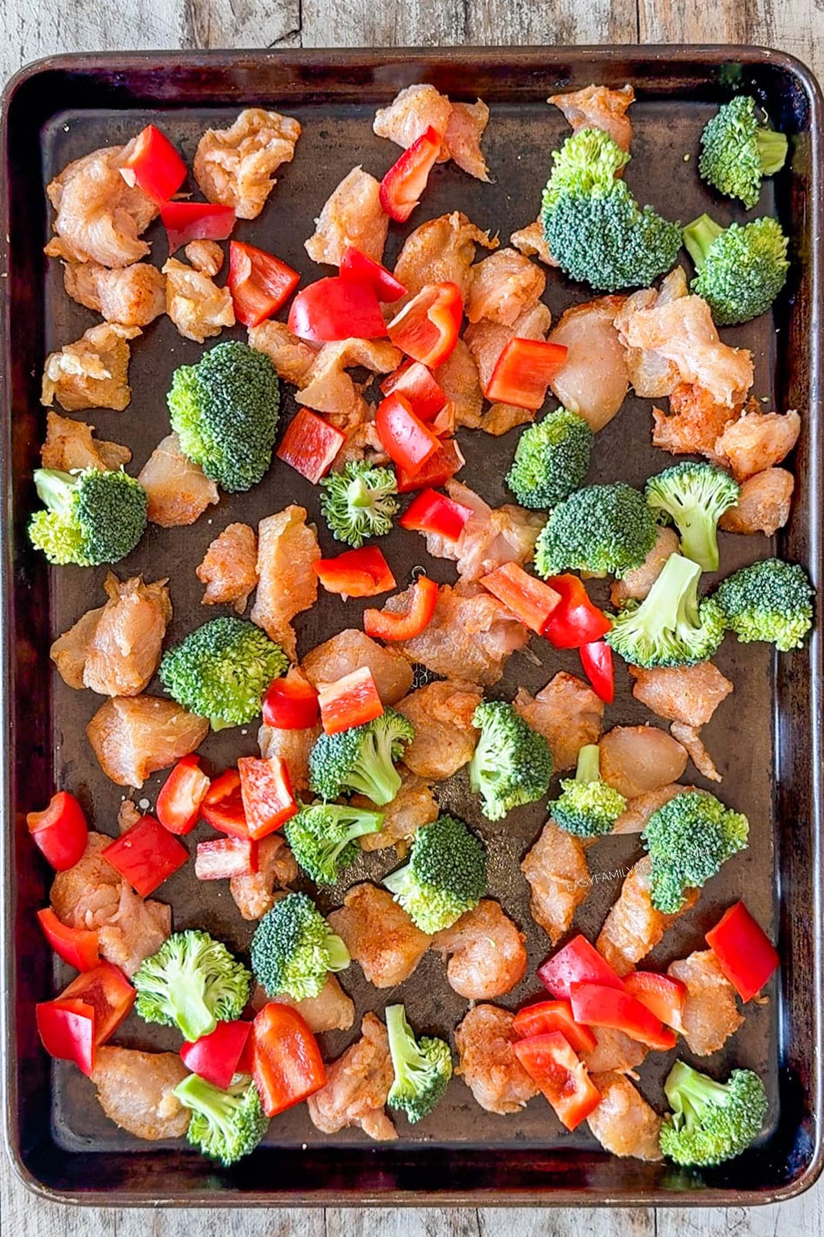 Seasoned chicken with vegetables placed on a sheet pan.