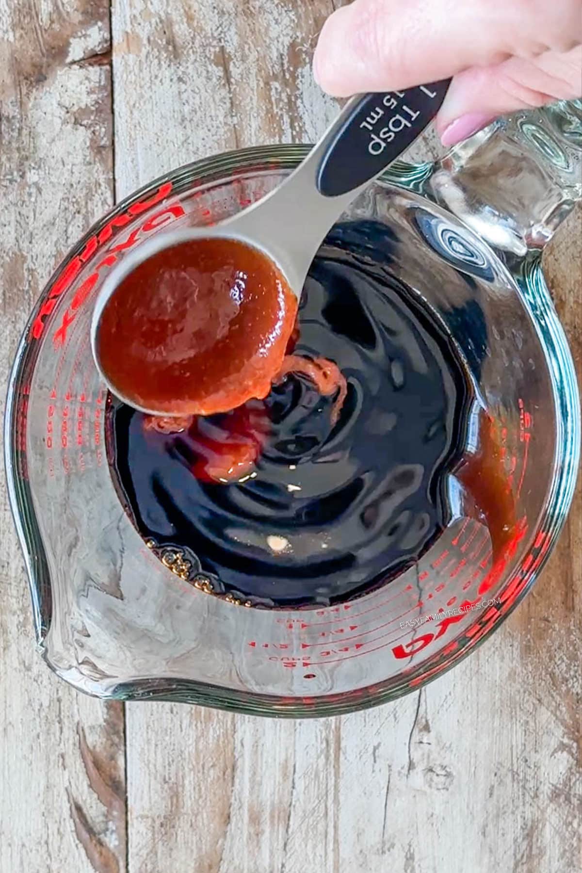 Hand using a measuring spoon to measure out the sauce ingredients.