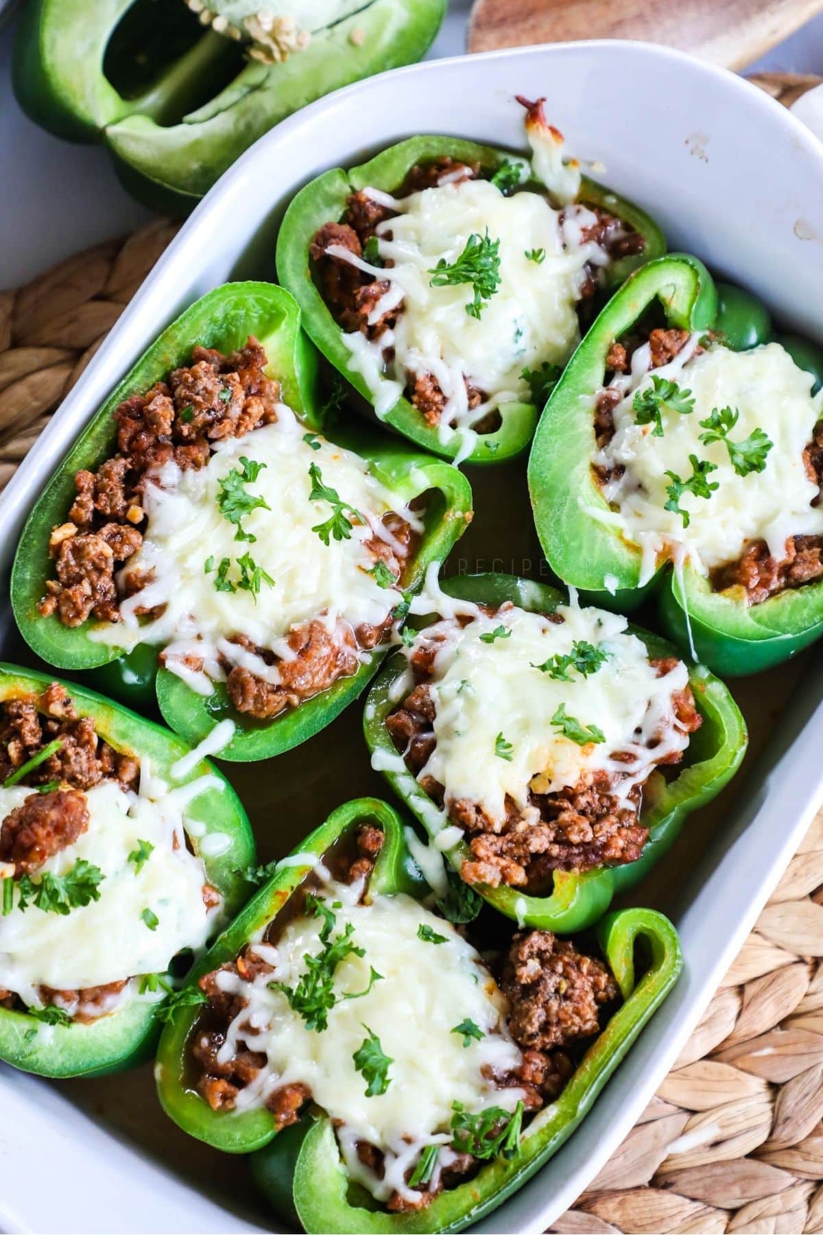 6 lasagna stuffed peppers topped with cheese in a white baking dish