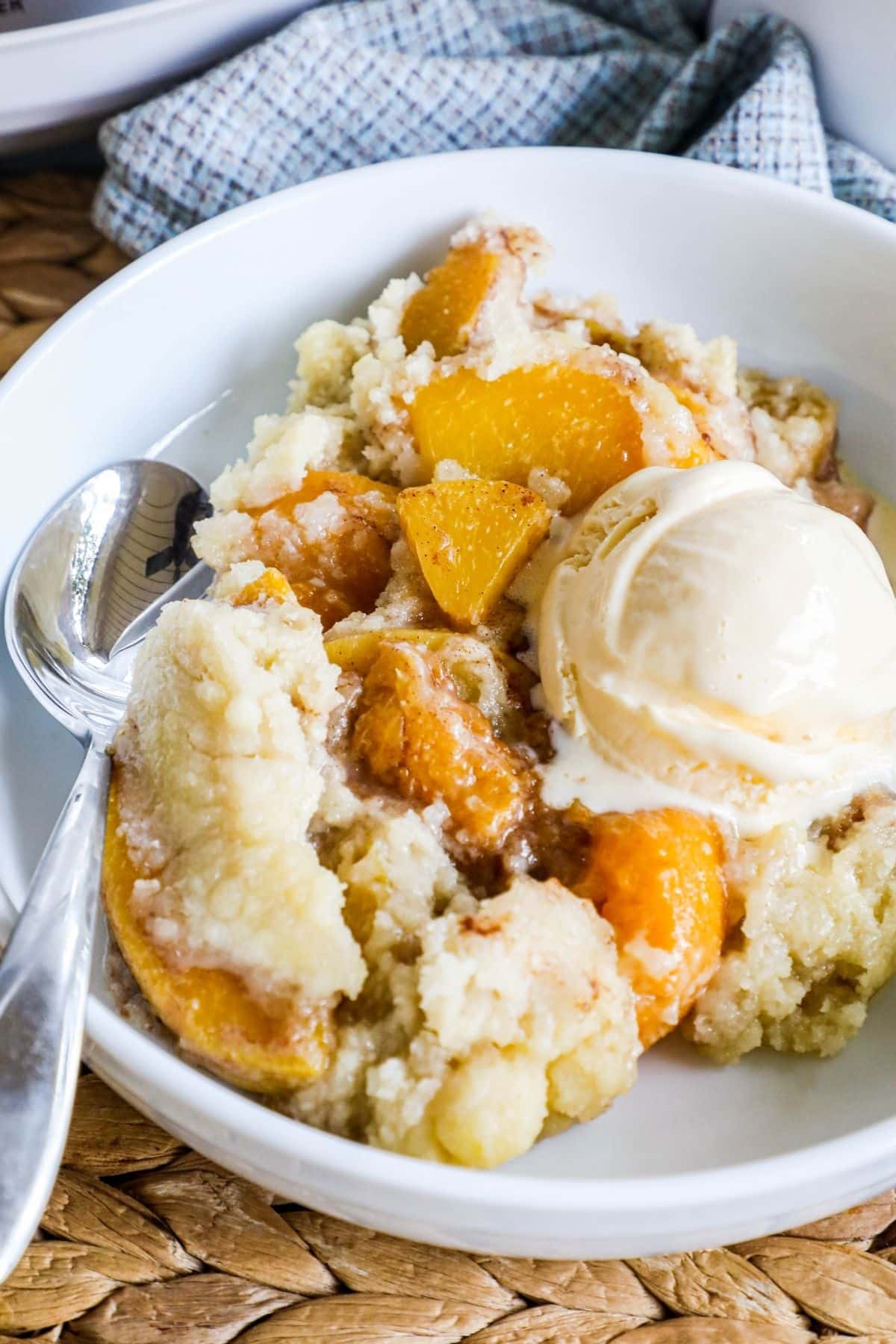 crockpot peach cobbler with a scoop of vanilla ice cream in a white bowl