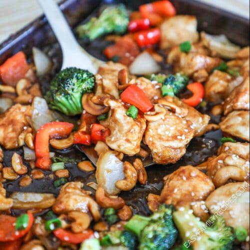 Sheet pan cashew chicken on the sheet pan with a spatula picking some up.