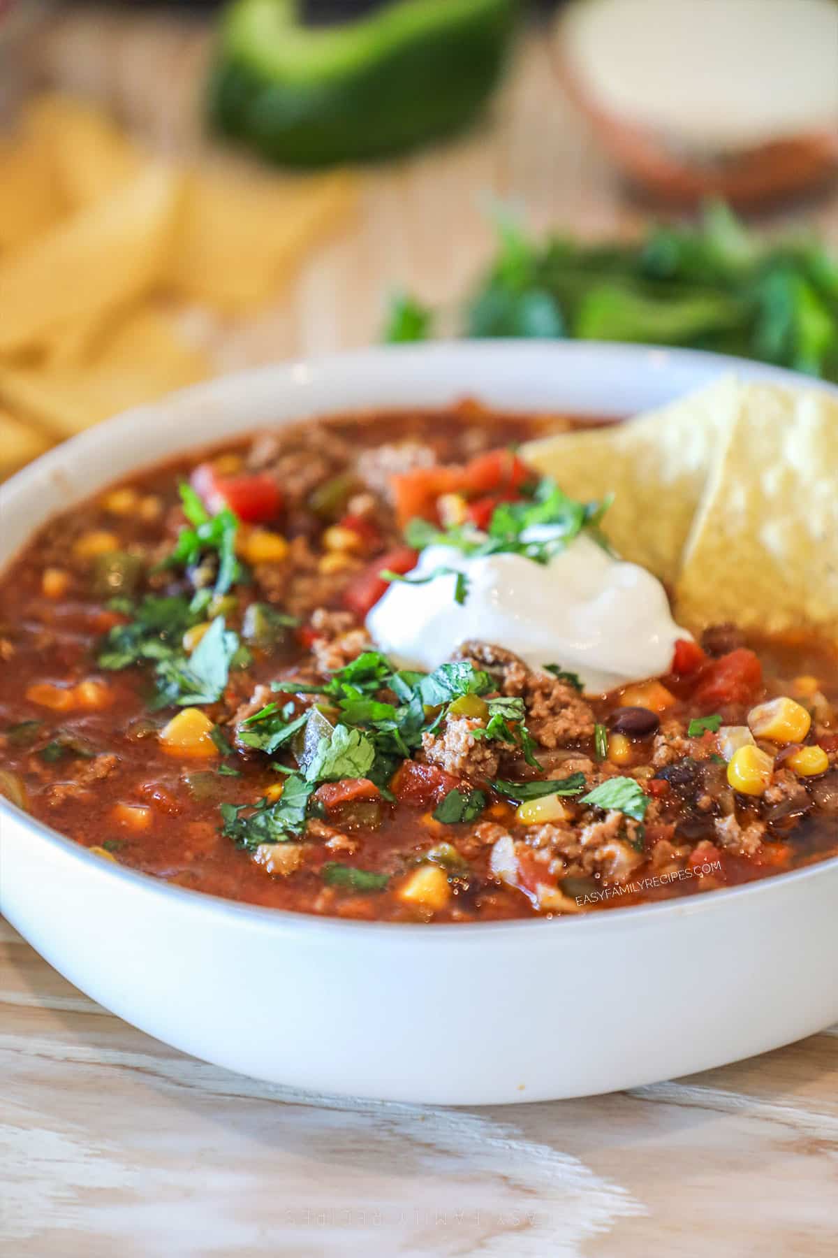 White bowl filled with Easy Crockpot Taco Soup, topped with a dollop of sour cream and two chips