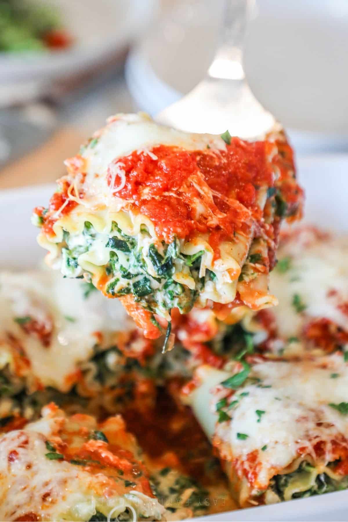 square of spinach lasagna roll up being lifted from baking dish on spatula
