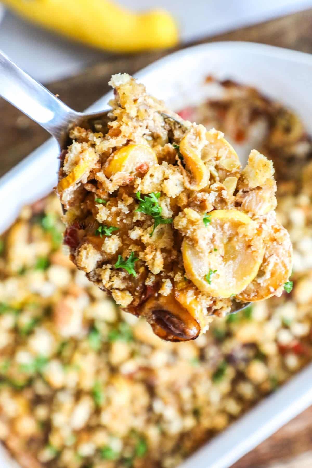 overhead shot of a scoop of squash casserole on a spoon over the casserole in a white dish