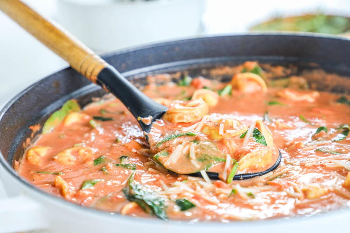 Tomato tortellini soup being scooped out of a large pot